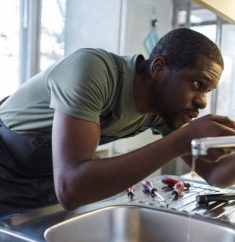 Photo of African American handyman in work clothes fixing leak in the kitchen sink