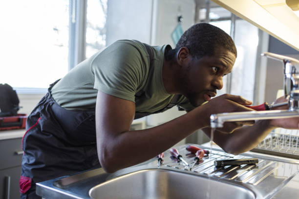 Photo of African American handyman in work clothes fixing leak in the kitchen sink